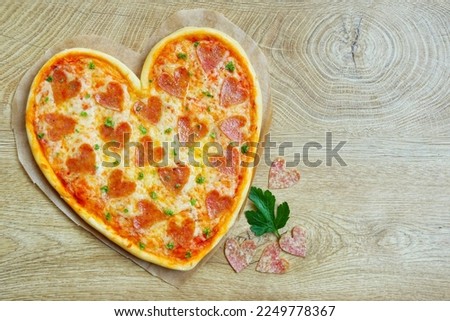 Heart shaped pizza with heart shaped salami on parchment paper with wooden background.Creative art food idea for Valentine or Mother day.Top view.Copy space