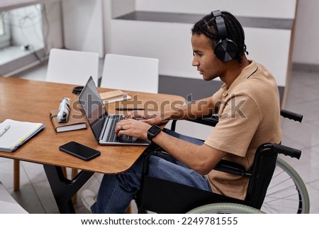 Portrait of black young man using laptop in college library and wearing headphones