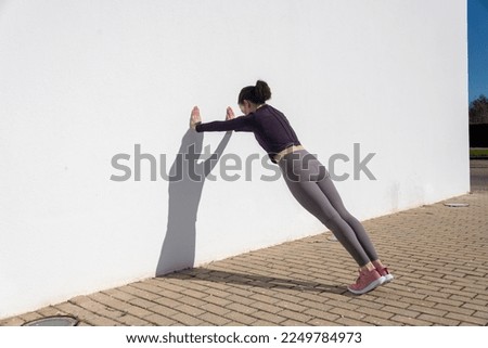 Sporty woman doing press ups against a white wall outside. Royalty-Free Stock Photo #2249784973