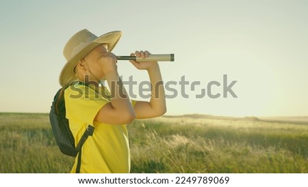 The child plays in nature in the traveler. A boy in a summer park in a hat looks through a spyglass in the summer outdoors. Kid, son, dreams of the discoverer of childhood fantasies. Children's travel Royalty-Free Stock Photo #2249789069