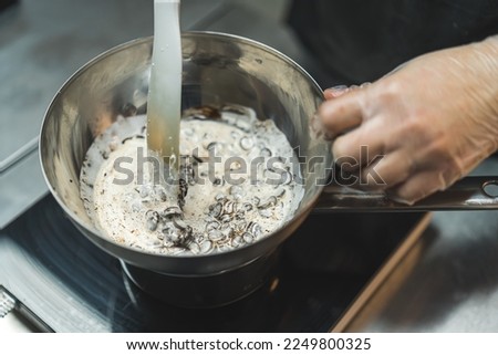 Close-up shot of unrecognisable baker melting chocolate with cream in water bath to prepare chocolate ganache. Professional baking process. Horizontal indoor shot. High quality photo