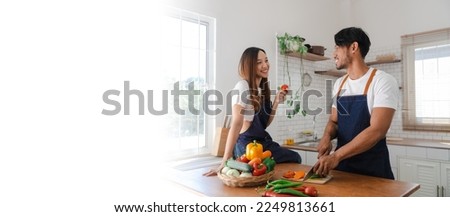 Happy asia young couple cooking together with vegetables in cozy kitchen, preparing vegetarian food colorful variety of vegetables and herbs lying on wooden kitchen table, love and valentine concept.