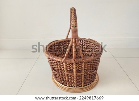 Rattan basket, round shape, li-shaped, brownish yellow  Placed on the tiled floor and white background wall, made of real rattan, with small and large rattan with meticulous hand weaving. Handmade.