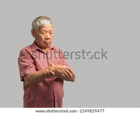 A senior man trying to hold his wrist while standing on a gray background. Causes of hand shaking Parkinson's disease, stroke, or brain injury. Mental health neurological disorder