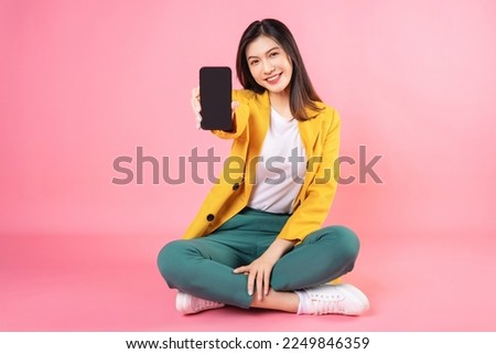 Image of young Asian businesswoman sitting and holding smartphone on background