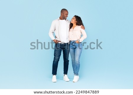 Full length shot portrait of black couple hugging and looking at each other, posing over blue studio background, full body length, free space