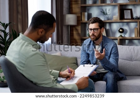 Visit to a psychologist. A man sits on a couch and talks to a psychotherapist. The patient is depressed, apathetic and stressed from problems in his personal life. Help of a psychologist. Royalty-Free Stock Photo #2249853239