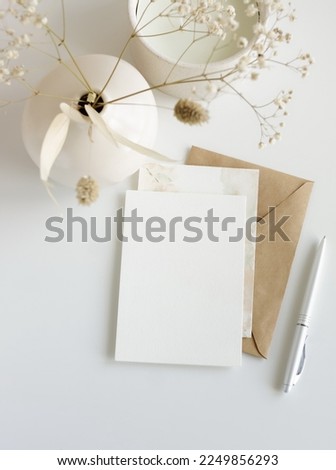 Greeting card mockup, envelope and  dried flowers in a vase on beige background top view flatlay. Card mockup with copy space.
