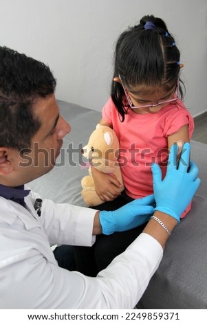 Dark-haired Latino doctor and little girl have a medical consultation in the pediatric office to vaccinate their arm against Covid, chickenpox, diphtheria, influenza, hepatitis, measles, mumps
 Royalty-Free Stock Photo #2249859371