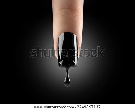 Nail art. Black gel polish dripping from beautiful long nail over black background. Woman finger with dark manicure and drop of nail polish. Fashion art design