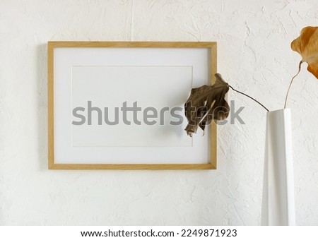 Portrait frame mockup with copy space for artwork, photo, painting, print presentation and dried leaves in a vase near white wall .