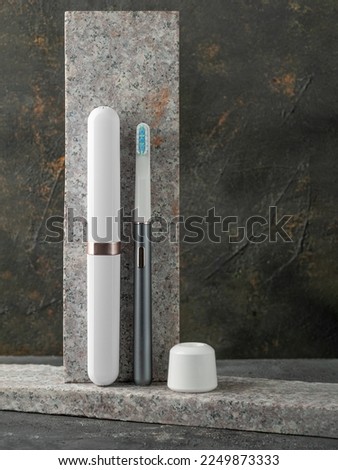 Modern sonic electric toothbrush. Made from gray metal. Storage case and charger nearby. Professional oral care and healthy teeth. Minimalistic design. Gray marble background.