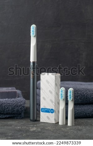 Sonic electric toothbrush. Made of gray metal. Nearby is a set of replaceable toothbrush heads of two pieces. On a gray background.