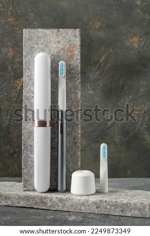 Modern sonic electric toothbrush. Made from gray metal. Nearby storage case, charger and replacement brush head Professional oral care and healthy teeth. Minimalistic design. Gray marble background.
