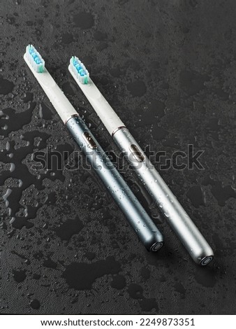 Modern sonic electric toothbrushes. Made from gray metal. Professional oral care and healthy teeth. Minimalistic design. They lie in the water. Black background.