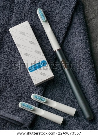 Sonic electric toothbrush. Made of gray metal. Nearby is a set of replaceable toothbrush heads of two pieces. View from above. Gray fabric background.