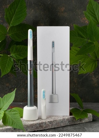 Modern sonic electric toothbrush. Made from gray metal. Nearby storage case, charger and replacement brush head Professional oral care and healthy teeth. Minimalistic design. Gray marble background.