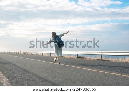 Rear view of young woman traveller with backpack walking on road. Japanese happy moody tone photography. Background with blue sky. Outdoor travel feel freedom.