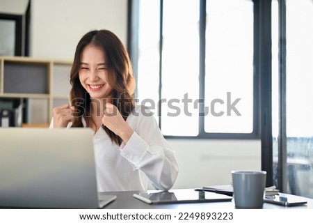 Successful and cheerful young Asian female office worker or businesswoman looking at laptop screen, celebrating her success, happy with her project's result, getting job promotion or new job offer. Royalty-Free Stock Photo #2249893223