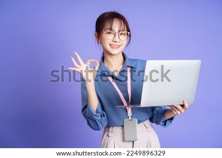 Photo of young Asian businesswoman holding laptop on background