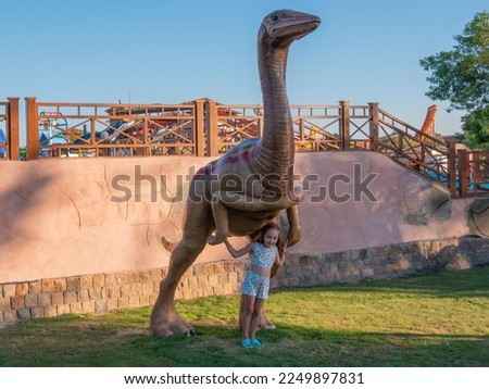 Little girl near a large brown dinosaur in the park on a sunny day.