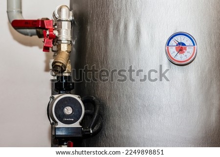 Pump, Storage Tank with Thermometer for Water Heating system at Home. Manometer, Buffer Tank, pipe, Valves of Heat system in Boiler room in House. Royalty-Free Stock Photo #2249898851