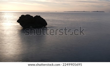 in the middle of the water appears the rock illuminated by the dawn.