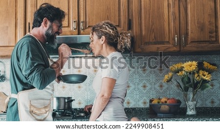 Young mature couple at home in love cooking lunch together. Good relationship in indoor leisure activity together cooking for dinner. Happy man and woman in the kitchen in domestic lifestyle. Romance Royalty-Free Stock Photo #2249908451