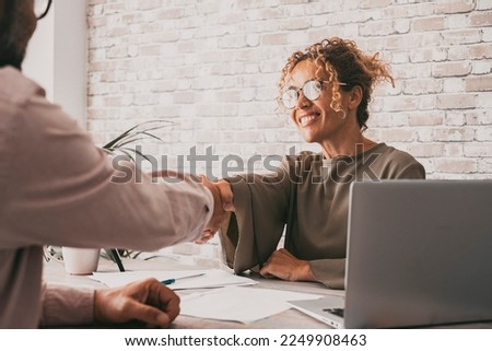 Happy woman and man signing agreement holding hands. Businesswoman and client at the desk closing contract with a smile. Confidence and business concept. Entrepreneur doing her job with happiness.