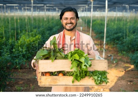 Happy smiling young farmer carrying basket of vegetables for market at green house - concept of successful business, confident and professional