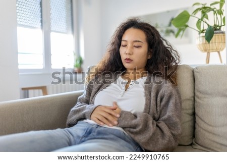 Asian woman lying on sofa looking sick in the living room. Beautiful young woman lying on bed and holding hands on her stomach. Woman having painful stomachache on bed, Menstrual period Royalty-Free Stock Photo #2249910765