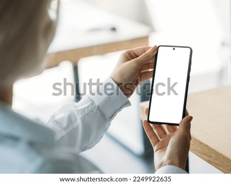 Online conference. Elegant woman. Mobile mockup. Unrecognizable lady looking smartphone with blank screen in light room interior.