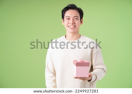 Image of young Asian man holding giftbox on background