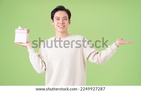 Image of young Asian man holding giftbox on background