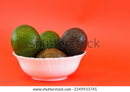 green avocado in a white bowl, on a red background.