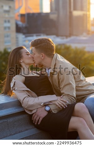 Young happy beautiful loving couple on a surprise romantic date on a rooftop on a Saint Valentine's Day. Attractive man and woman, male and female hugging, kissing. Sunset, skyscrapers urban view