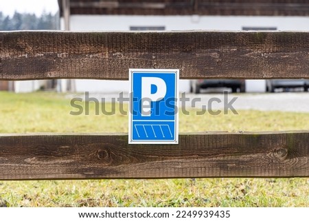 The Parking place for cars and the blue sign on the wooden fence