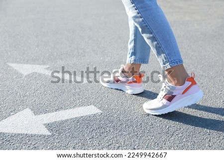 Choice of way. Woman walking to drawn mark on road, closeup. White arrows pointing in different directions