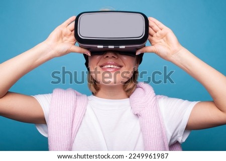 Young caucasian woman using VR headset, touching glasses and looking up in virtual reality on blue background. Digital technology entertainment. Modern