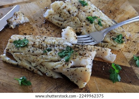 A Fork Of Baked Cod Fillet Garnished With Black Pepper And Parsley.