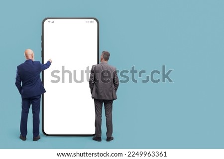 Business people standing in front of a big smartphone with blank screen, they are using mobile apps