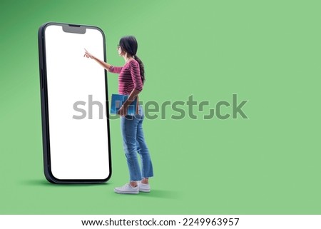 Female student holding notebooks and using a big smartphone with blank screen, e-learning concept, copy space Royalty-Free Stock Photo #2249963957