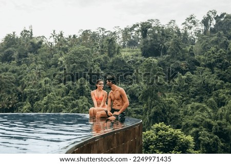 Portrait of young couple sitting together in pool enjoying holiday. Happy young romantic couple relaxing in swimming pool