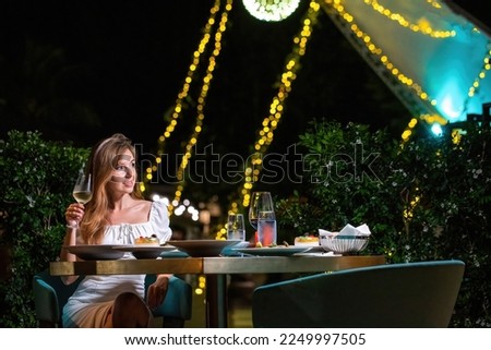 Elegant Young Woman in White Dress Enjoying Champagne at Evening Dinner in Luxury Restaurant. High-end dining experience. Fine dining and luxury lifestyle Royalty-Free Stock Photo #2249997505