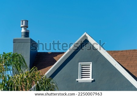 Dark blue stucco house facade or exterior with white accent paint on roof edge and visible chimney and vent on house Royalty-Free Stock Photo #2250007963