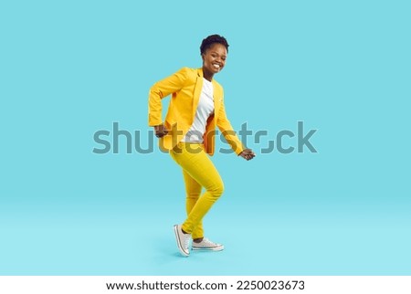 Full body shot of happy cheerful joyful beautiful young African American woman in bright yellow suit and white T shirt dancing isolated on blue color background. Fashion, party, having fun concept Royalty-Free Stock Photo #2250023673