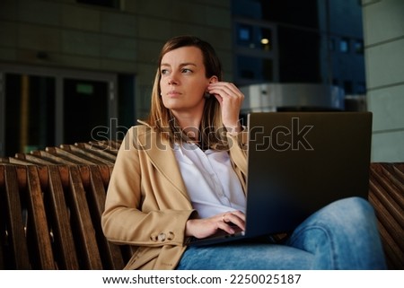 Woman sitting on bench outdoors and using laptop. Concept of remote working and online education.