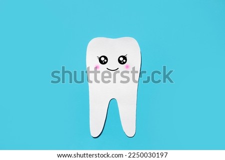 Silhouette of a healthy white tooth with a funny muzzle on a blue background. Flat lay, space for text. Children's tooth treatment concept.