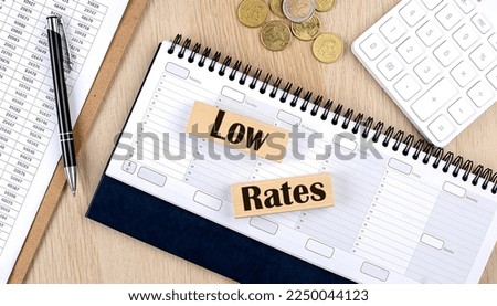 LOW RATES word written on a wooden block on planner with coins, clipboard and a calculator