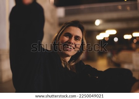 Attractive woman with a lovely smile making a frame gesture with her fingers framing her face. Woman posing on selfie photo looking at camera walking outdoors in urban city at night or evening.